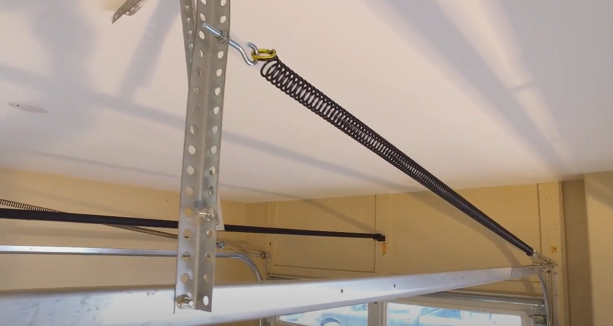 Technician in a branded uniform repairing a garage door track using specialized tools in a clean and organized garage in Bradenton, FL.